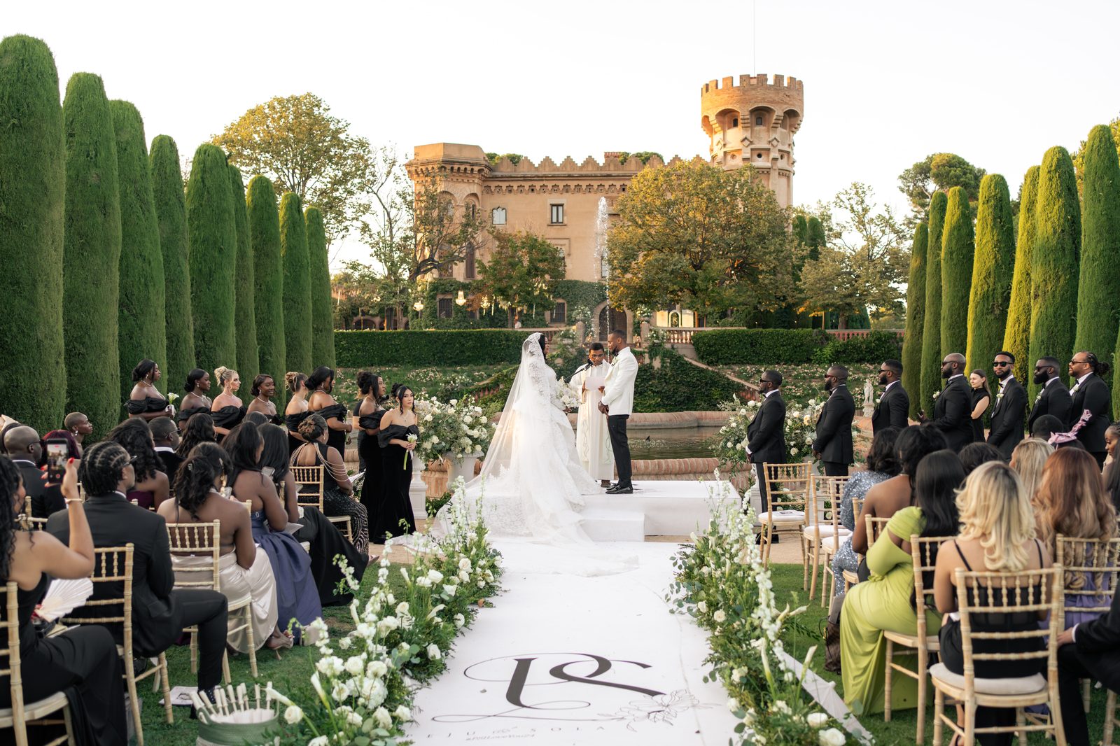 Peju & Sola — ceremony with PS monogram aisle and Castell de Sant Marçal in the background