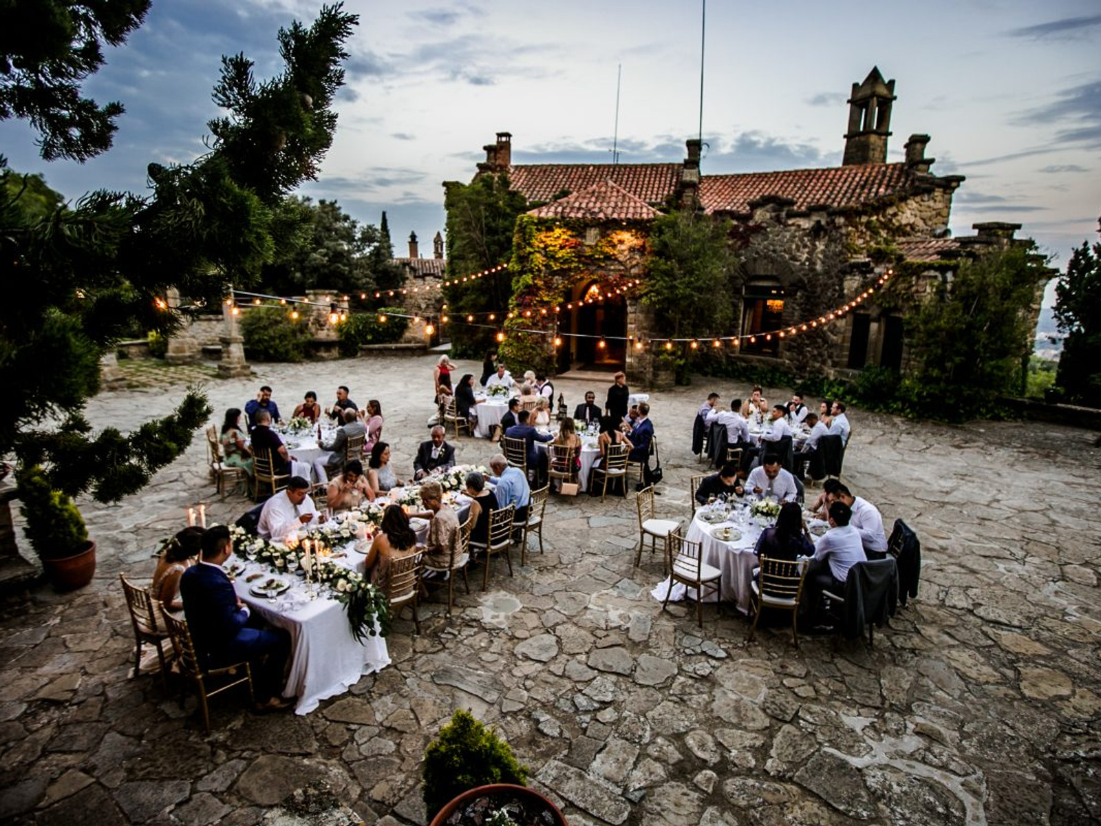 Wedding guests enjoying an outdoor cocktail reception on the stone patio of La Baronia, showcasing the grand historic facade and elegant garden atmosphere.